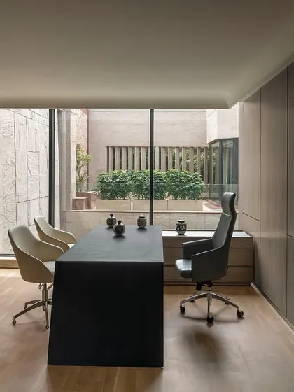 A meeting space within a director's cabin at 'The Layered Office'. The sleek, modern desk and chairs are positioned to take advantage of the view into the private courtyard, blending indoor and outdoor environments.