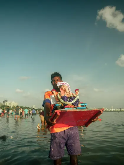 A lone devotee carries a small Ganesh idol into the sea for immersion, with the Mumbai skyline in the background. This shot contrasts the personal act of faith with the vastness of the city and the sea.