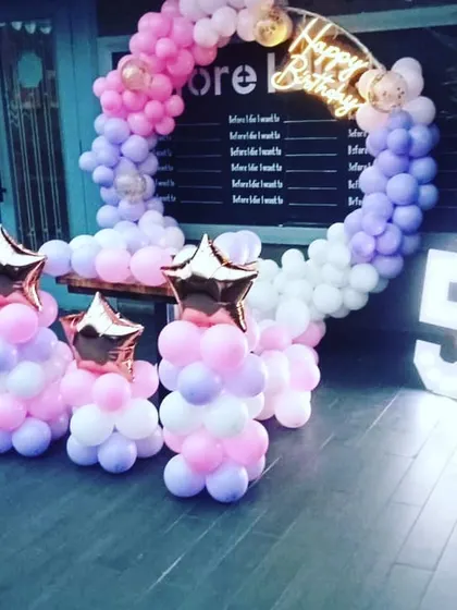 A pastel-colored balloon ring for a 5th birthday. This setup includes star-shaped foil balloon columns and a large light-up number '5', perfect for an outdoor or cafe party.