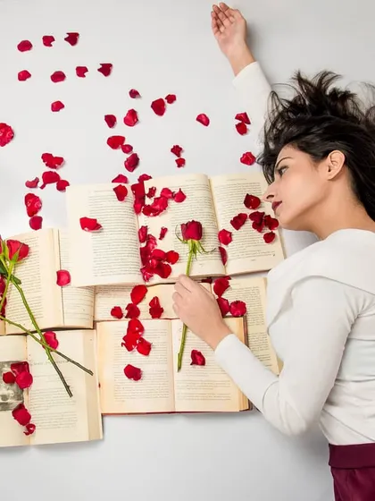 An overhead shot from the 'Bittersweet Memories' series. The model lies among scattered book pages and red rose petals, creating a visually poetic scene about love and heartbreak.