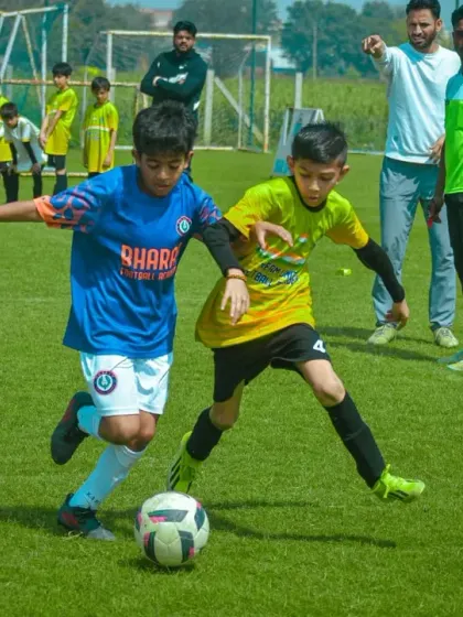 Coaches and referees watch on as two players compete for the ball, ensuring a fair and developmental environment.