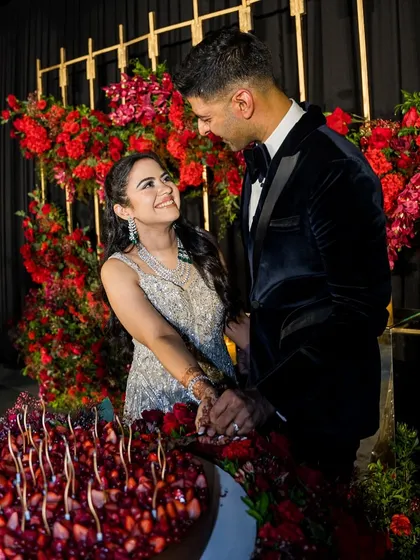 This is a photo from my own wedding. Sharing a smile with my husband as we cut our custom-made berry and chocolate cake, surrounded by a beautiful red floral arrangement.