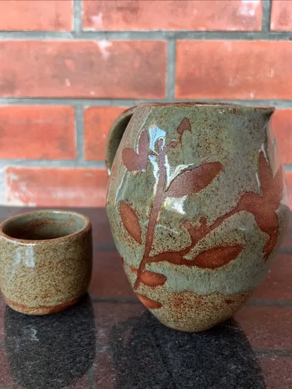 This rustic pitcher and cup set was made by a student and decorated with a leaf motif using a wax-resist technique.