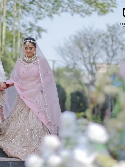 A full-length shot of the couple descending stairs, capturing the flow and elegance of the bride's pastel pink lehenga and the groom's coordinated sherwani.