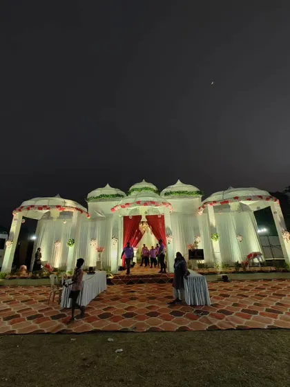 A straight-on shot of the completed dome-style wedding venue at night. The combination of white drapes, red accents, and warm lighting creates a classic and welcoming look for guests.