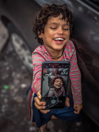 A joyful, heartwarming shot of a young boy laughing as he holds up a phone displaying his own picture, a beautiful moment of self-discovery.