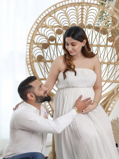 Here, the dad-to-be lovingly gazes at his partner, who is seated on a peacock chair. Her simple white gown and the bohemian decor create a relaxed and stylish maternity look.