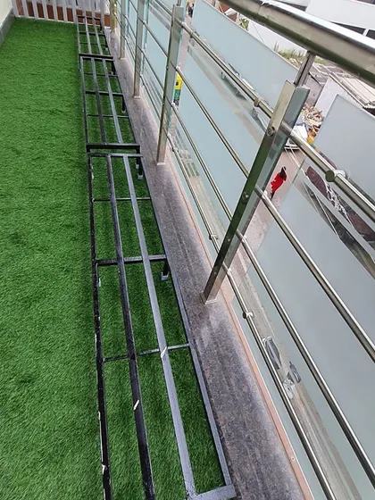 This shows the metal stands placed on top of the newly laid artificial grass, ready for the pots. The combination creates a clean, organized, and lush balcony garden.