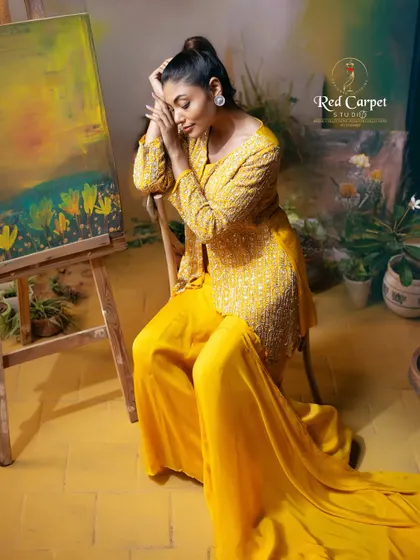 A model posing artistically in a vibrant yellow embroidered jacket and palazzo set. The image captures the feeling of fashion as a form of art.