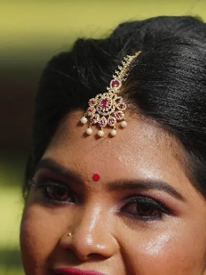 A detailed shot of the bride's maang tikka and hairstyle. The hair is styled in a clean updo to beautifully showcase the traditional jewellery piece.