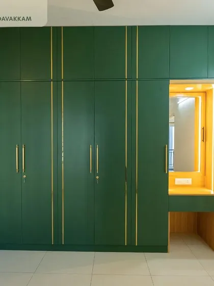 A master bedroom in Casagrand Zenith featuring a floor-to-ceiling wardrobe in a rich forest green, accented with sleek golden strips and handles, and an integrated dressing unit with profile lighting.