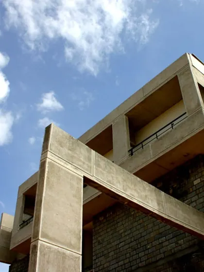 An upward shot of the curved hostel block, highlighting the strong geometry of the concrete structure against the sky. The material choice connects the building to the campus's modernist roots.