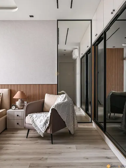 This angle shows the full-length mirrored wardrobe, which makes the room feel larger and brighter. The comfortable armchair creates a perfect reading nook in the corner.