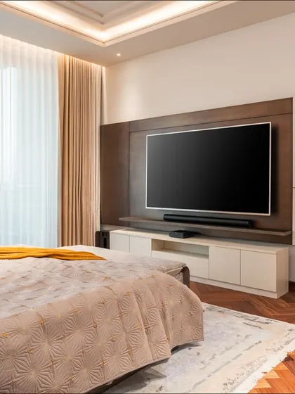 The TV and media unit in this master bedroom is designed with a mix of veneer and lacquered finishes. The floating shelves and clean lines maintain a minimalist aesthetic while providing practical storage.