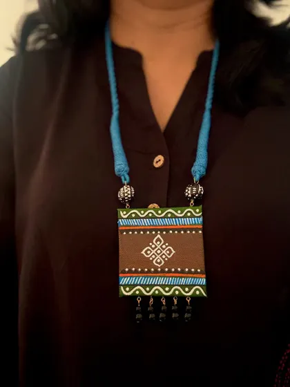 An elegant rectangular pendant with a hand-painted design featuring an eternal knot symbol. The combination of brown, green, and blue gives it a sophisticated, earthy feel.