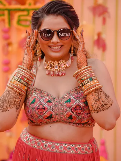 The bride is all smiles, showing off her "Team Bride" sunglasses during her Mehendi ceremony. This is a fun, candid shot that captures the bride's personality and the festive mood.