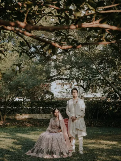 A formal, editorial-style portrait. The couple is posed in a lush garden, looking directly at the camera, creating a stately and elegant image reminiscent of a classic painting.