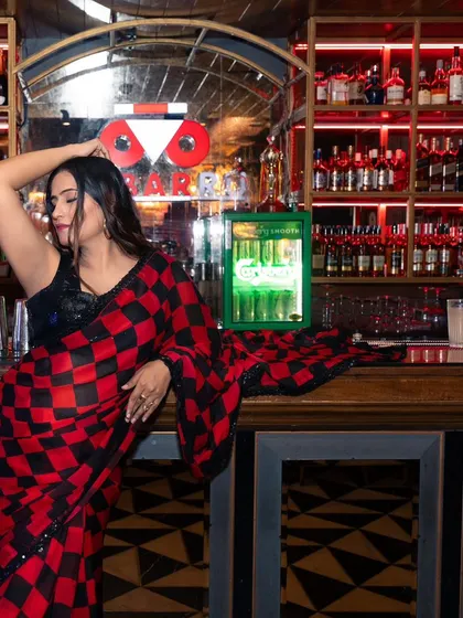 A wide shot of a model in a saree, leaning against a well-lit bar. This image showcases the entire outfit and the ambiance of the location, perfect for a brand's lookbook.