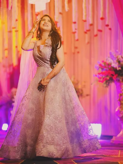 A candid, joyful shot of a client wearing a light purple gown at a wedding event. The dress has a subtle shimmer and a flowing silhouette, perfect for dancing the night away.