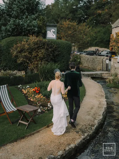 The newly married couple takes a private stroll along the river, a quiet moment of connection amidst the beautiful English garden setting.