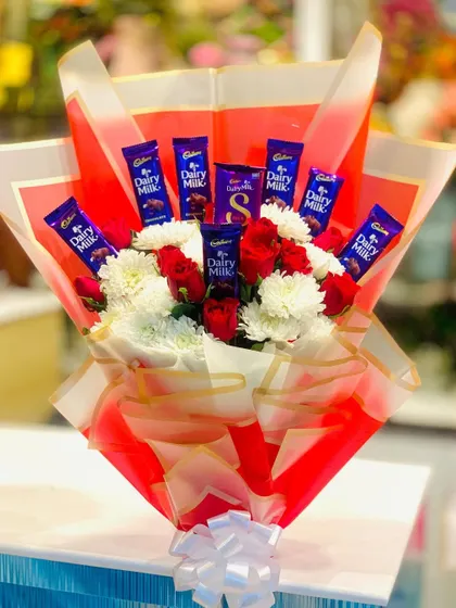 A vibrant bouquet combining fresh flowers with chocolates. This design features red roses and white chrysanthemums surrounded by bars of Cadbury Dairy Milk, all wrapped in bright red paper.