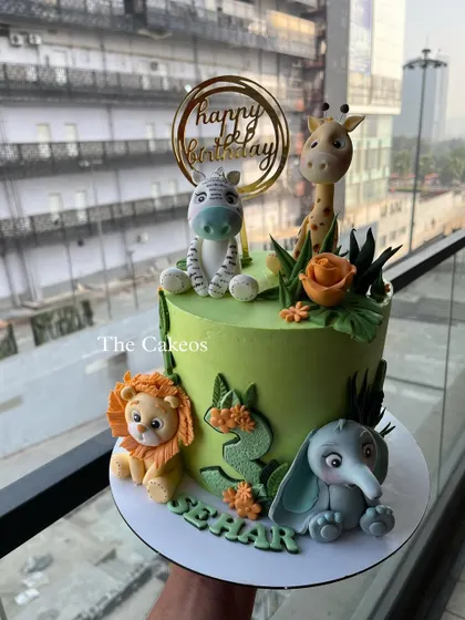 A bright green jungle cake surrounded by four fondant animals. This design is perfect for a safari-themed party, featuring a lion, elephant, giraffe, and zebra.