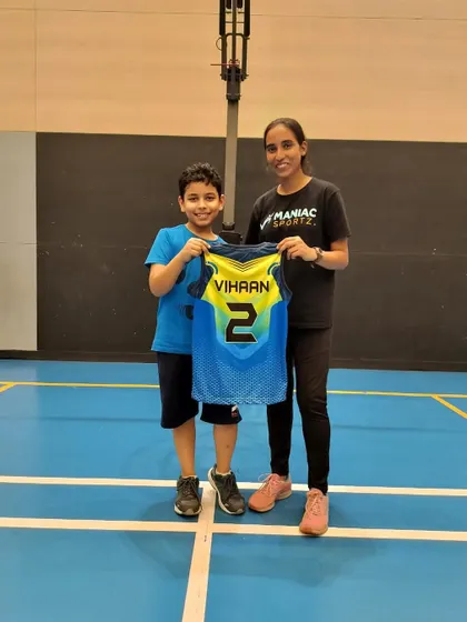Officially welcoming Vihaan to the Maniac family! A coach and a new young player proudly hold up his personalized jersey.