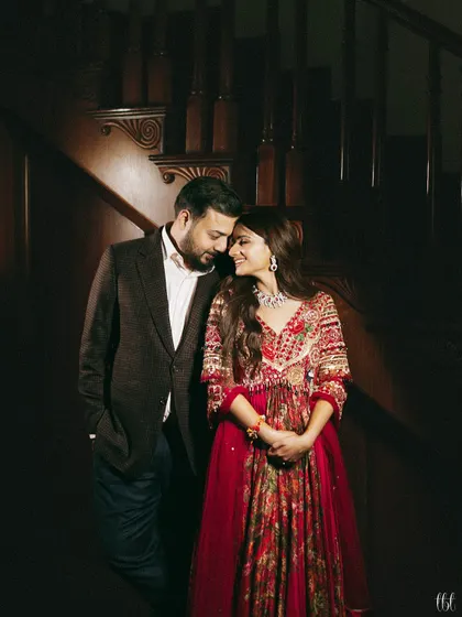 A romantic portrait of the couple on a staircase. Her red Gazal Gupta anarkali and his classic suit create a timeless and elegant look for their pre-wedding dinner.