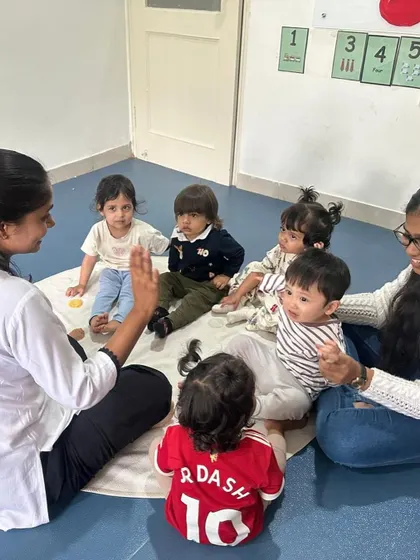 Toddlers and teachers sit in a circle for a group activity, learning social skills like taking turns and listening to others.