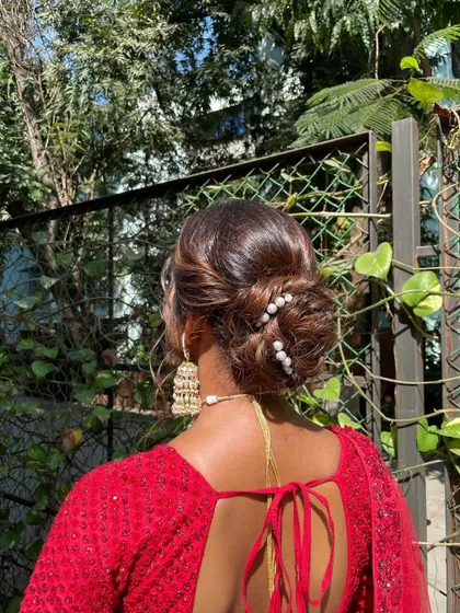 A modern take on the bridal bun, this textured updo is accented with scattered pearls. It’s a chic and sophisticated hairstyle for a bride in a contemporary red lehenga.