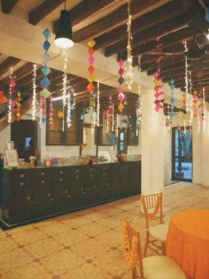 An indoor mehendi setup with colorful paper hangings and warm lighting. This decor is perfect for creating a festive and playful daytime vibe.