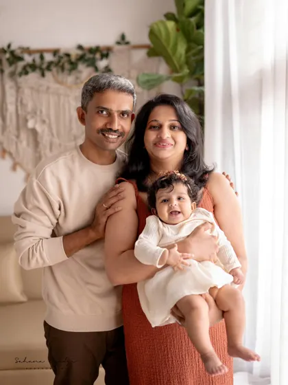 A happy family portrait in a cozy, plant-filled studio. The baby girl's bright smile is the centerpiece of this lovely photo.