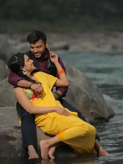 A relaxed and romantic photo of a couple sitting by the river, their feet dipped in the water.