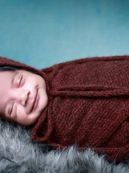 A sweet, smiling newborn wrapped in a deep brown swaddle, resting on a soft fur blanket. The rich, warm tones are perfect for creating a cozy atmosphere.