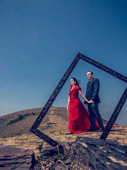 A creative pre-wedding shot where a couple is framed by a large, empty picture frame on a hilltop. This shows our use of props and concepts to create unique and memorable images.