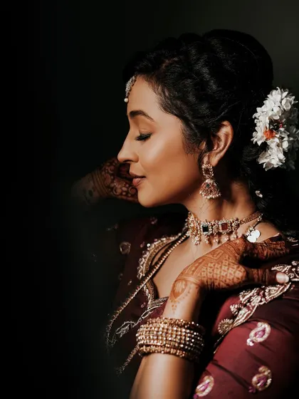 A side profile of the client, highlighting her jewelry and the intricate mehendi on the back of her hand.