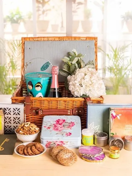 This hamper combines treats and keepsakes for the couple's new home. It includes cookies, nuts, teas, a mini champagne bottle, and decorative tins, all presented in a charming picnic basket.