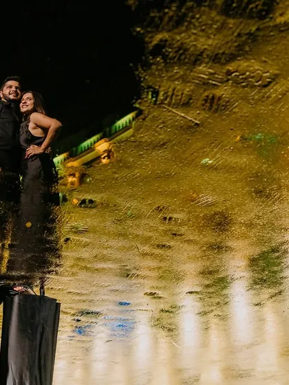 Using a puddle from the Mumbai monsoon, I created this artistic reflection shot. The couple stands against the dark night while the city lights paint a golden, abstract pattern on the water's surface.