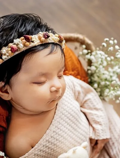 A peaceful newborn nestled in a rustic basket, surrounded by baby's breath and holding a tiny teddy. These posed shots are perfect for capturing their angelic features.