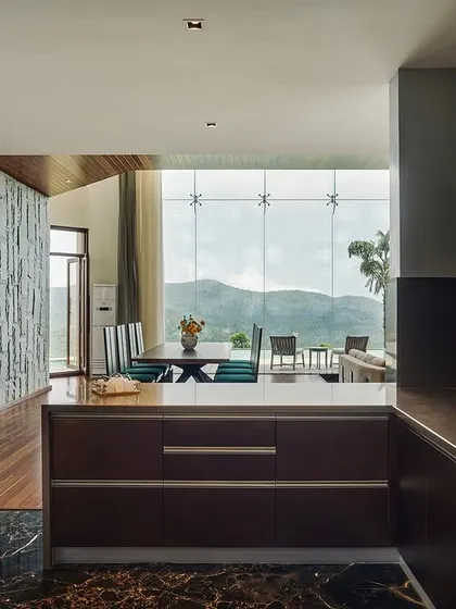 The open-plan kitchen and dining area overlook the mountains through a floor-to-ceiling glass wall. The design combines rough stone textures with sleek, modern cabinetry, reflecting our blend of rustic and contemporary styles.