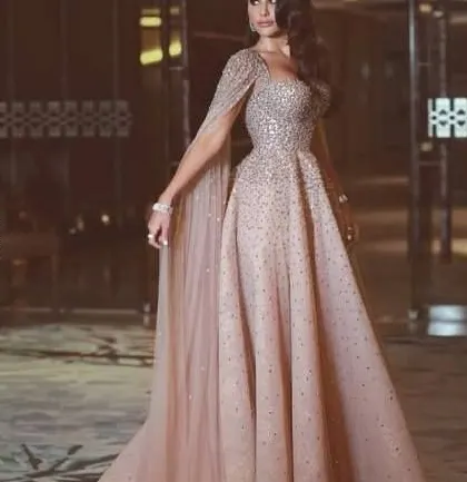 A fairytale gown for your special event. This blush pink dress features a sparkling, embellished bodice and a full tulle skirt, with an attached cape for added drama.