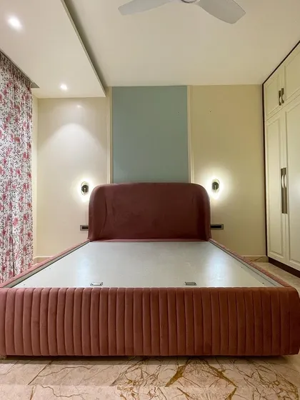 We call this the 'Rose Room'. The design is centered around a dusty rose upholstered bed with vertical tufting. The color palette is soft and calming, with a mint green accent panel behind the bed.