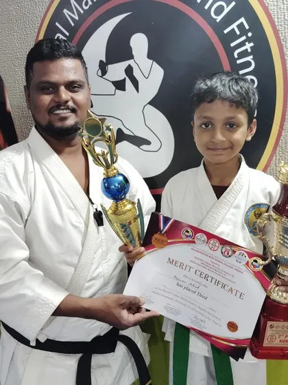 This young karateka holds his third-place certificate and trophies, celebrating his hard-earned spot on the podium.