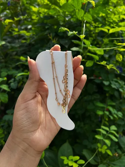 A delicate, personalized initial anklet held against a natural green background, showcasing one of the jewelry options for my Rakhi hampers.