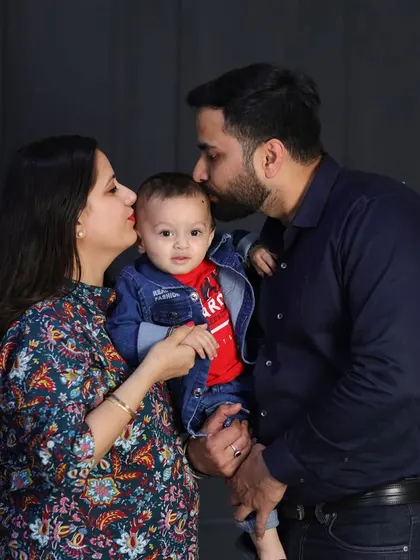 A tender moment between parents and their son. The father's kiss on the baby's head is a sweet, candid gesture that adds warmth to this classic studio portrait.
