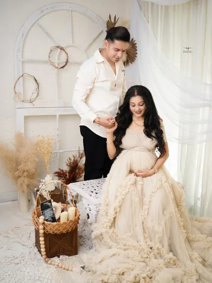A gentle and loving pose. The father-to-be holds his partner's hand as she sits gracefully, both sharing a quiet moment of connection.