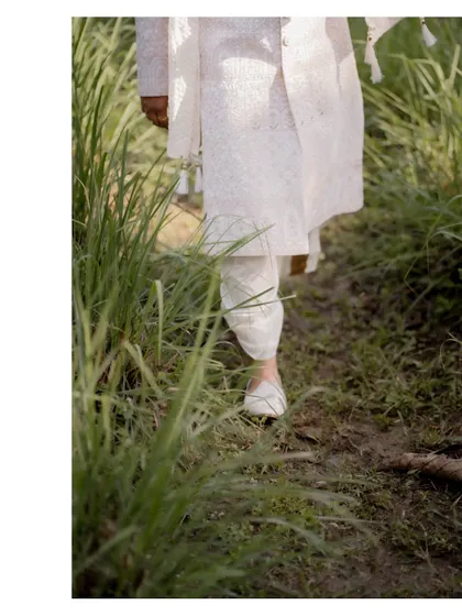 A detail shot of the groom's traditional footwear as he walks through the grass, a unique perspective on the wedding day.