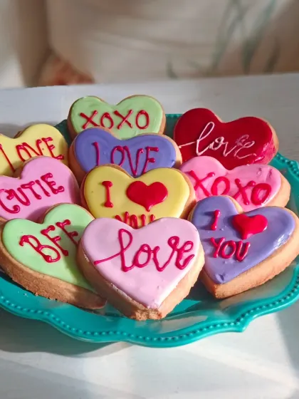 A colorful assortment of heart-shaped "conversation cookies" for Valentine's Day. Each cookie is hand-iced with classic messages like "Love," "XOXO," and "I ❤️ You."