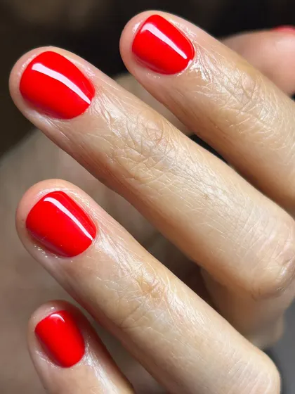 A vibrant, classic red manicure on short, natural nails. The high-gloss finish and precise application make this a standout look.