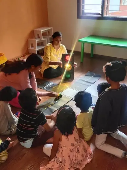 A group of children gathered for a discussion about traffic rules. Using a model traffic light and toy cars makes the lesson engaging and helps them understand important life skills for being safe citizens.